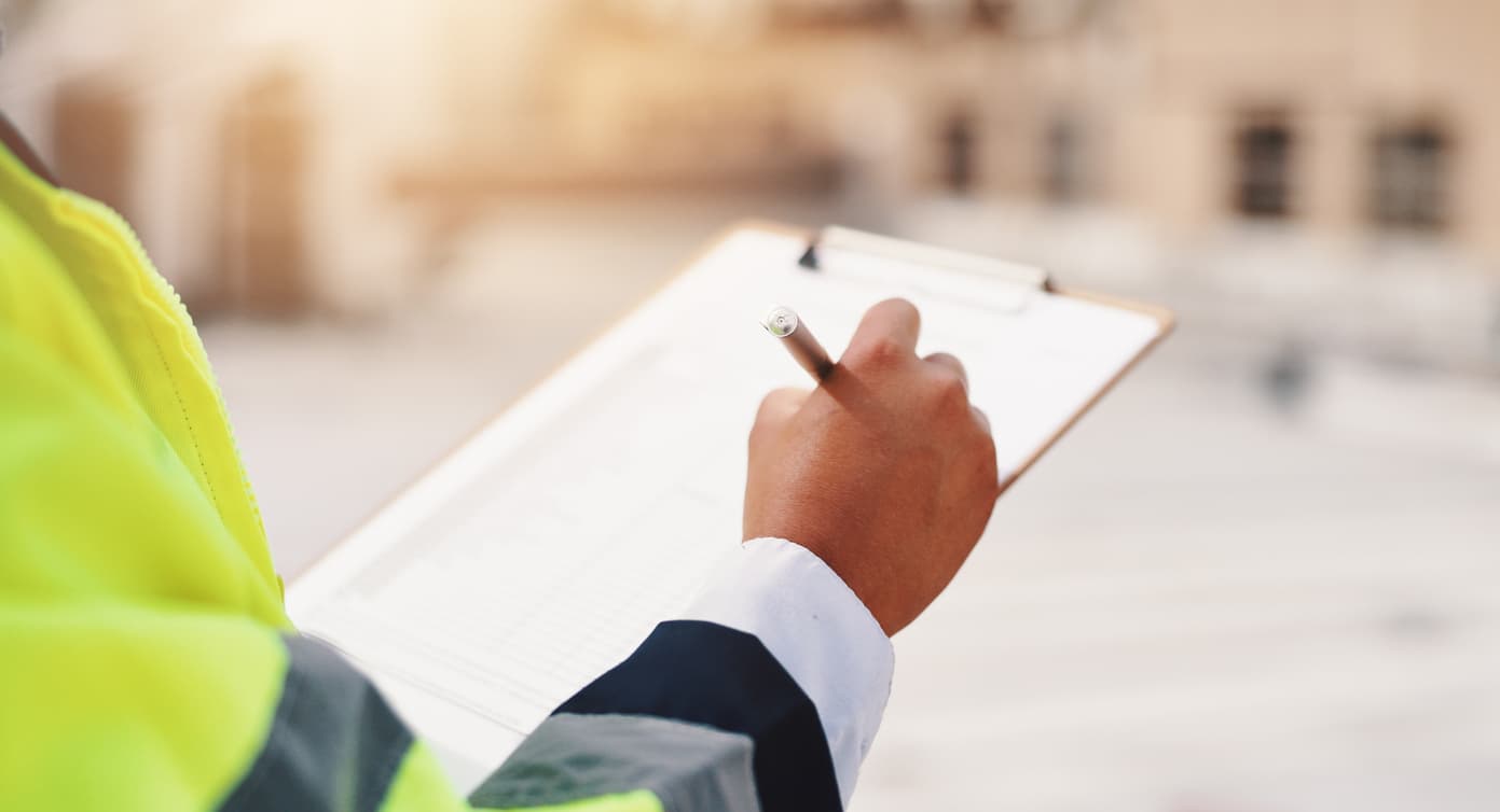 A close up photograph of a checklist is shown on a clipboard with a mans hand holding a pen over it