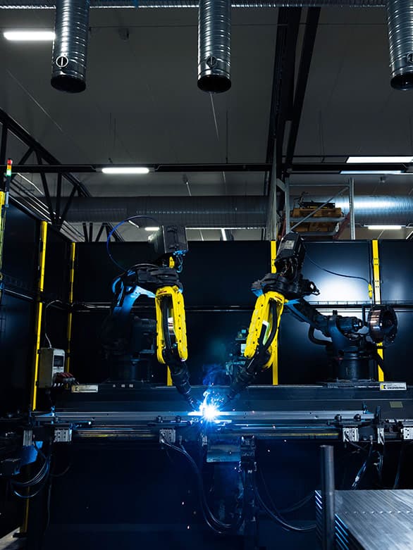 Automated welding robots operating in an industrial facility, enclosed by safety fencing. This image highlights compliance with international safety standards such as ISO, ANSI, and EN, ensuring workplace safety in robotic manufacturing environments.