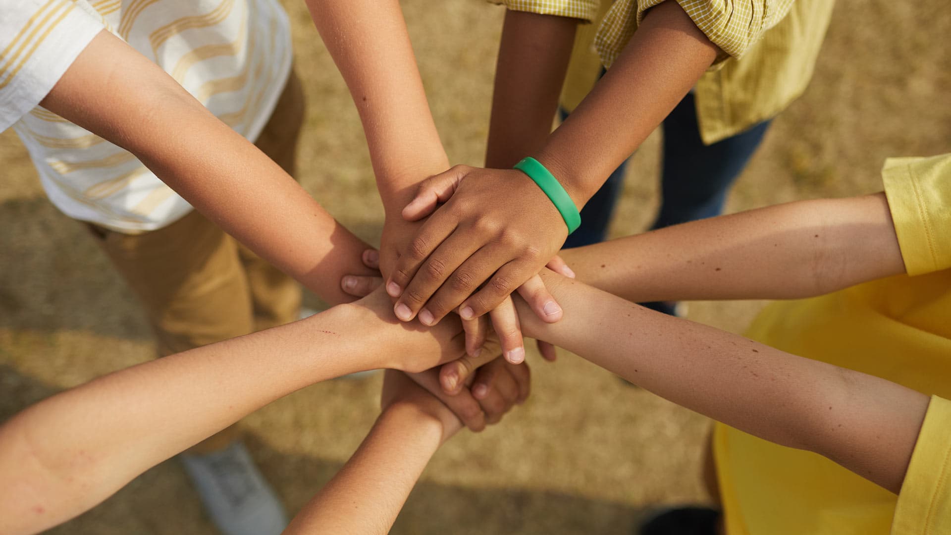 Children stacking their hands on top of eachothers while standing in a circle
