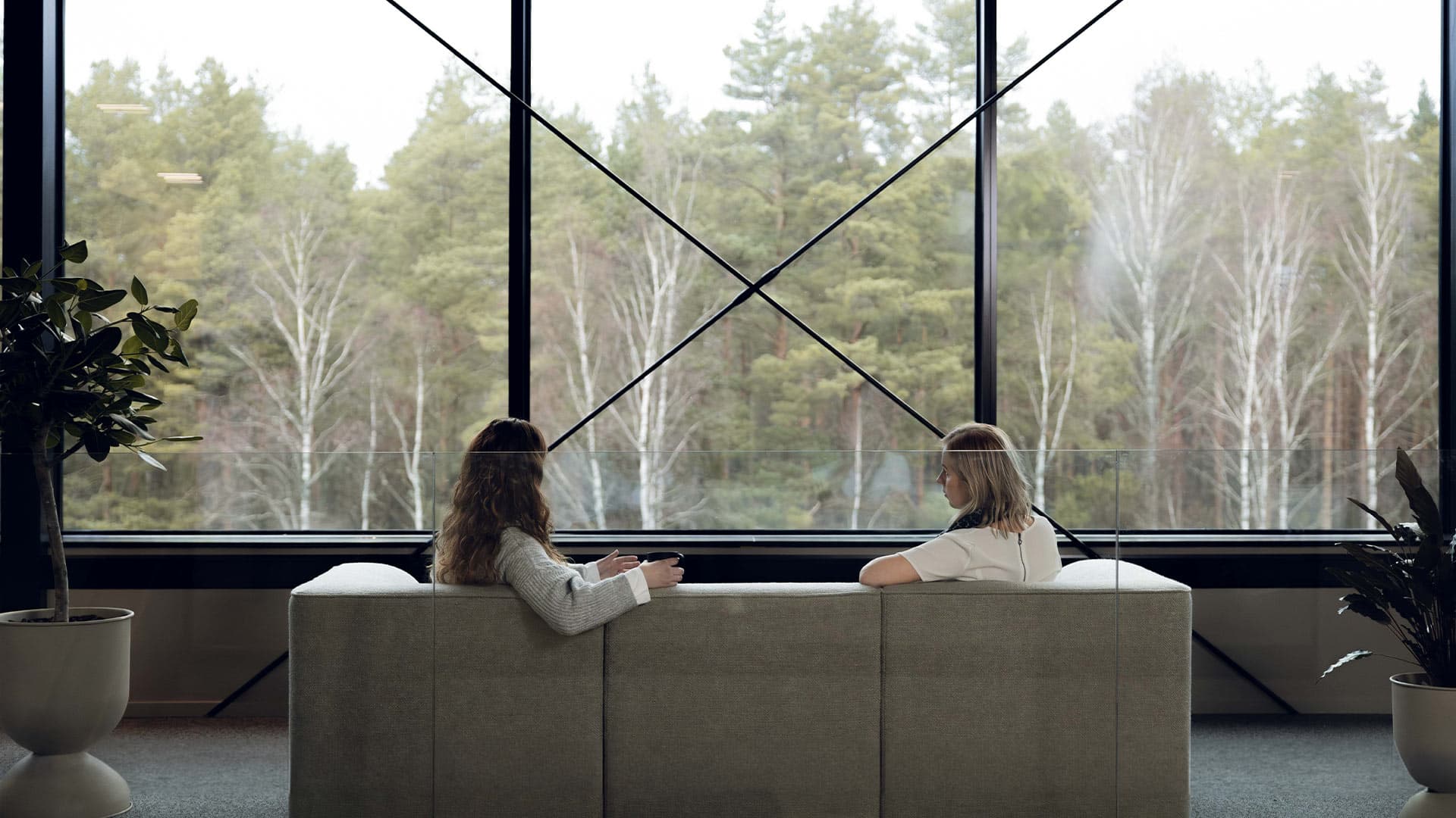 Two women sitting in a sofa facing a forest while talking to eachother