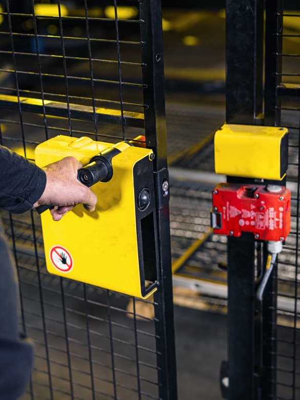 A worker opening a machine safety gate with a secure locking mechanism in an industrial setting. The image highlights key considerations when selecting machine guards, such as accessibility, durability, and compliance with safety standards.