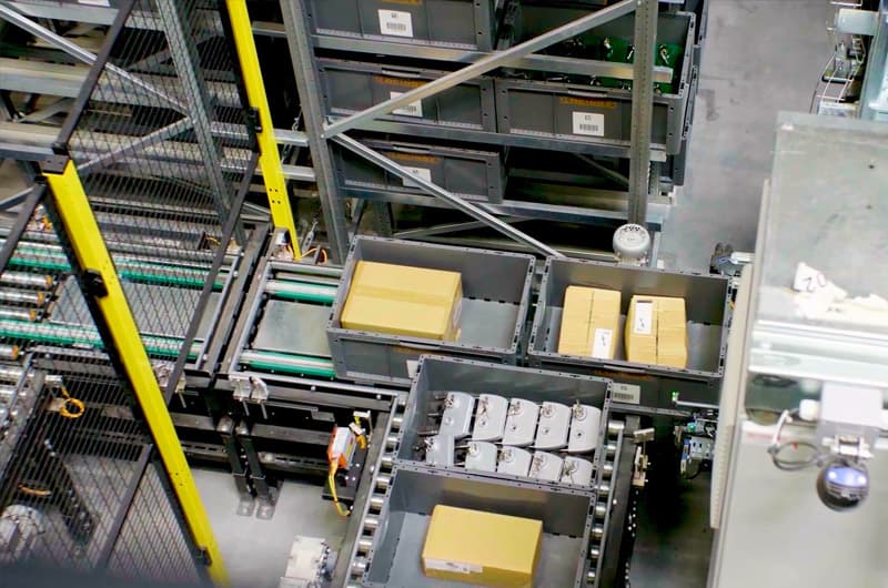 Automated material handling system with conveyor rollers and bins transporting packaged goods