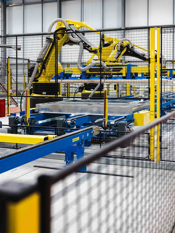 Automated yellow robotic arms operating within a safeguarded industrial workspace, enclosed by black and yellow safety fencing. These advanced robotic systems enhance manufacturing efficiency while ensuring compliance with machine safety standards. The protective barriers prevent unauthorized access, reducing workplace hazards.