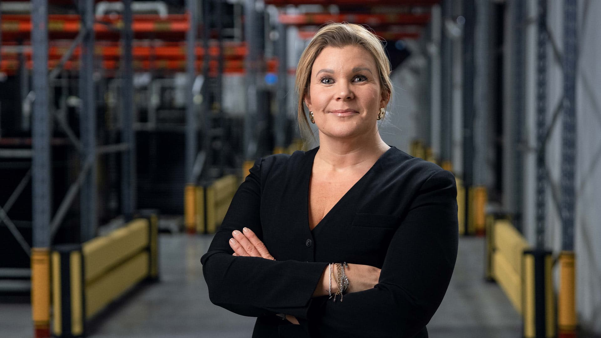 Axelent's CEO Karin Sandén Ahlqvist standing with crossed arms in a warehouse aisle smiling at the camera