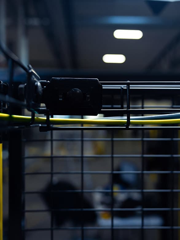 Close-up of an industrial guard fence with a yellow protective bonding cable attached. The image highlights the importance of grounding machine guards to prevent electrical hazards and ensure worker safety in industrial environments.