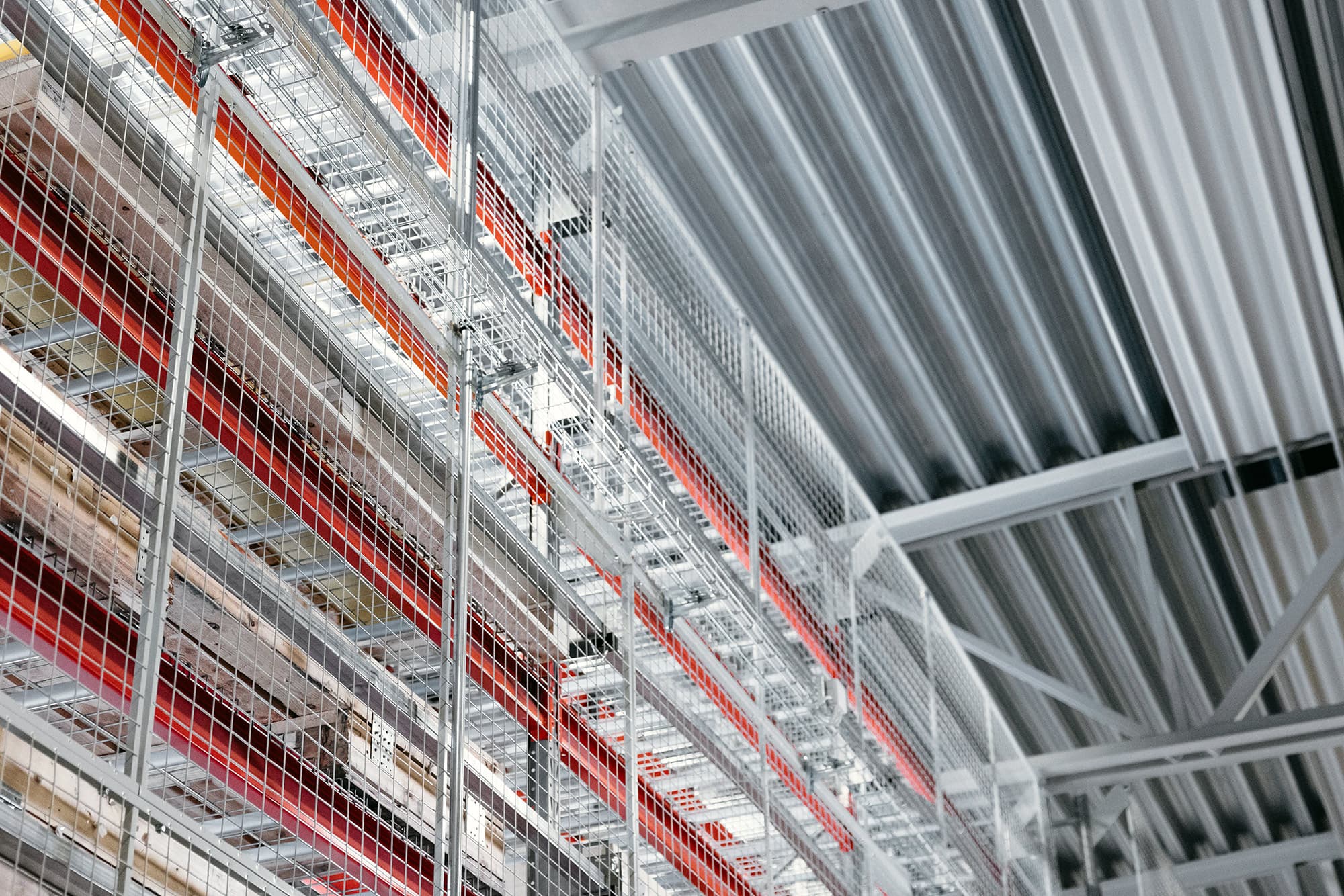 Tall warehouse racking system with wire mesh panels and overhead industrial ceiling structure