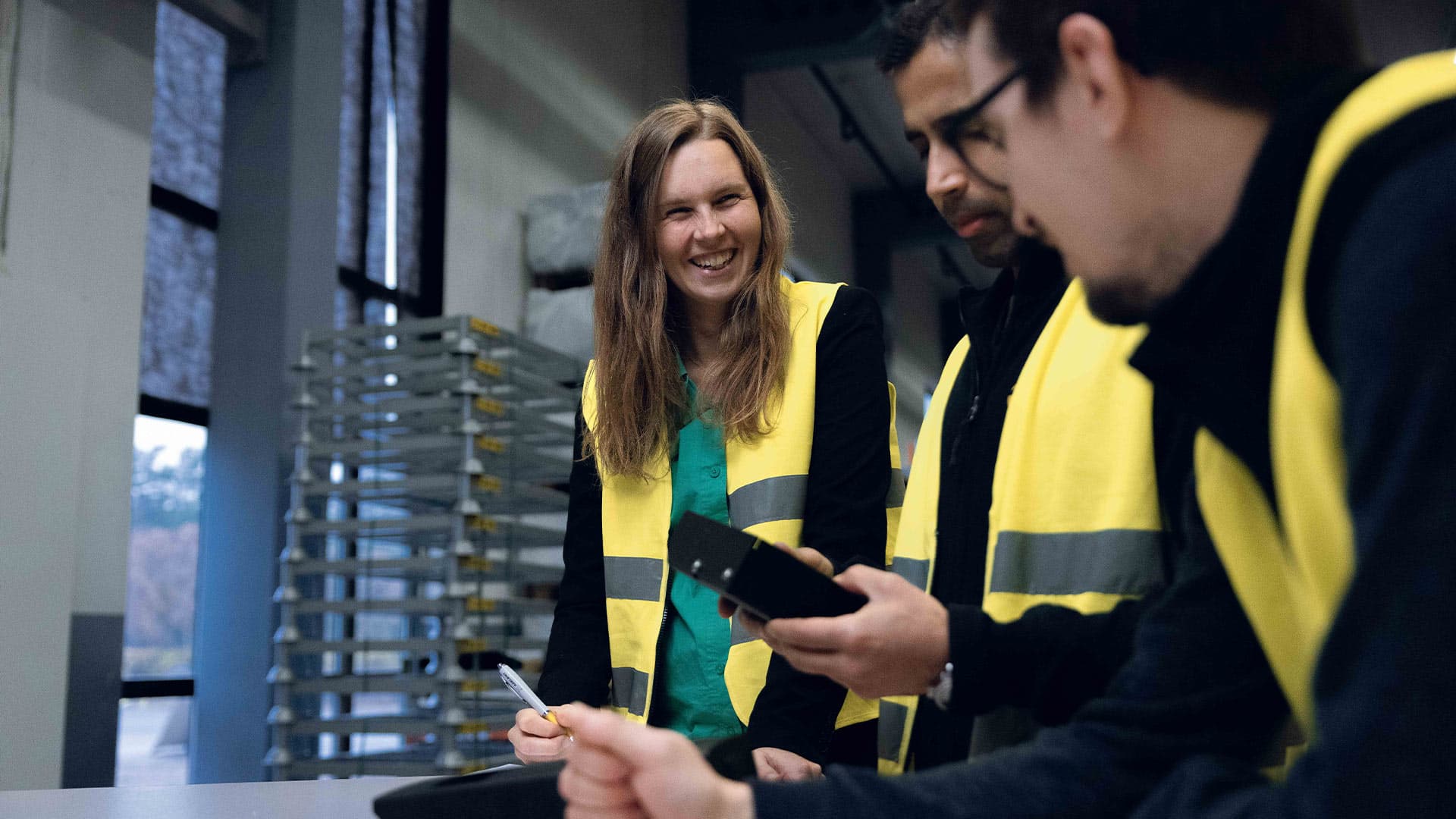 Employees wearing high-visibility vests discussing work tasks in an industrial environment