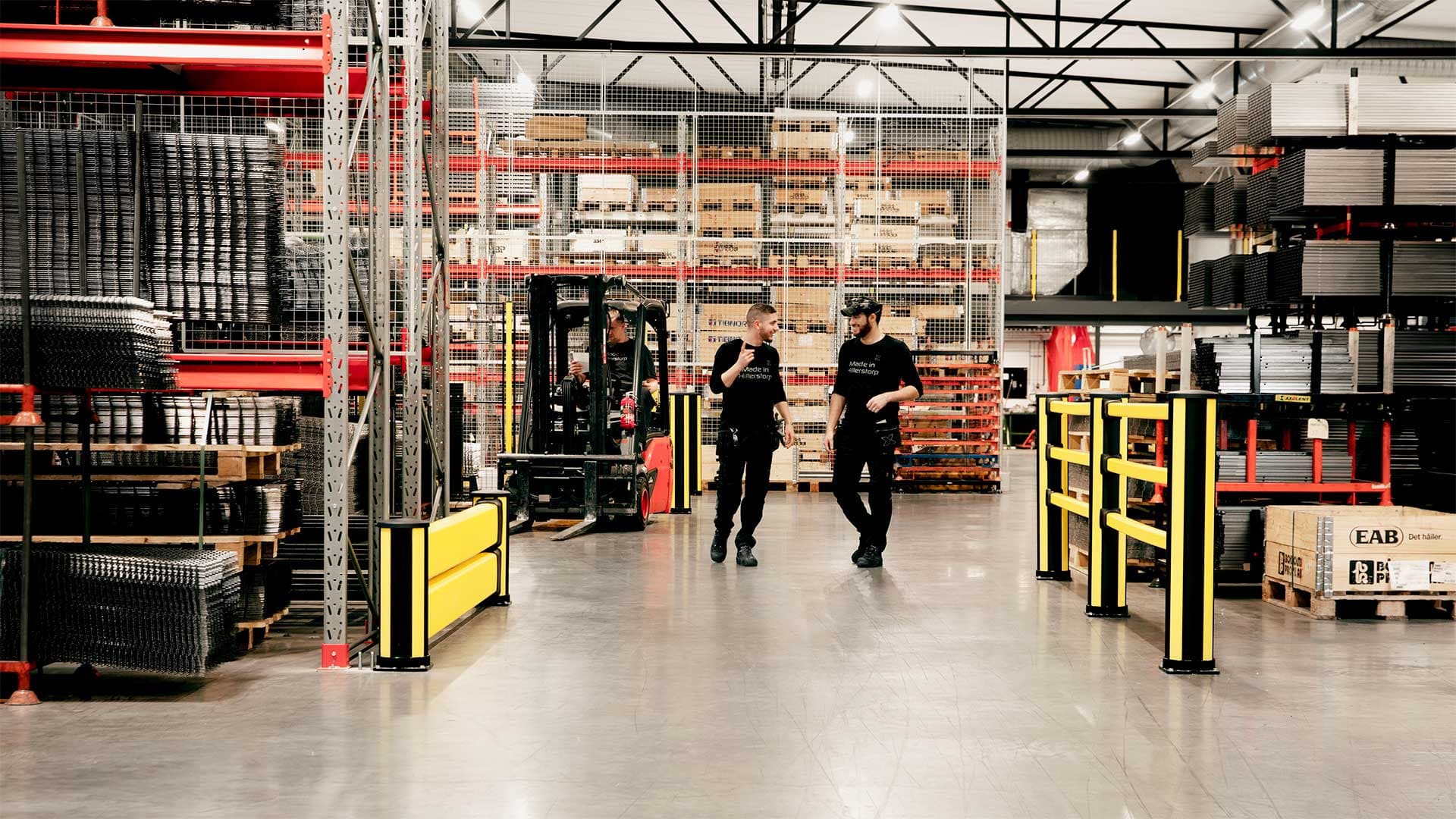 Industrial warehouse with workers walking safely behind yellow crash barriers, while a forklift operates nearby. The impact protection barriers ensure pedestrian and vehicle separation, enhancing workplace safety and compliance with industrial safety regulations for accident prevention.