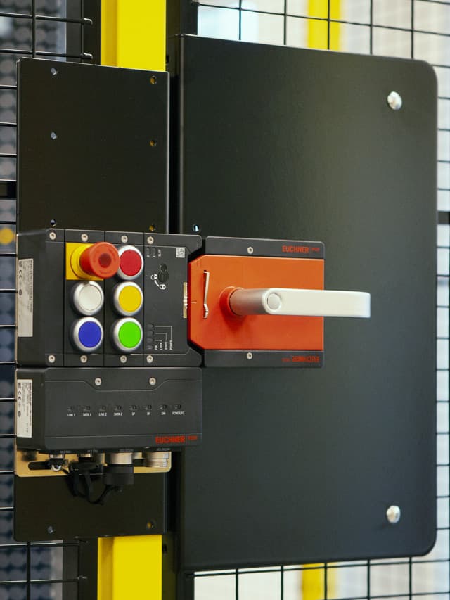 A safety switch system mounted on an industrial guard fence, featuring a secure locking mechanism and a control panel with emergency stop buttons. The image highlights the importance of selecting the right safety switch for machinery access control and worker protection.