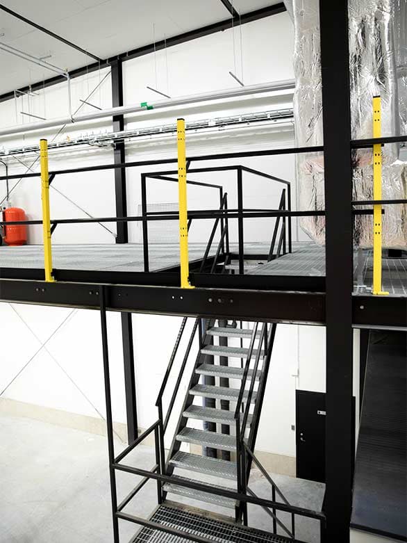 Industrial mezzanine with metal stairs and yellow fall protection guardrails, ensuring workplace safety at elevated work areas. Proper safety barriers help prevent falls and comply with industrial safety standards.