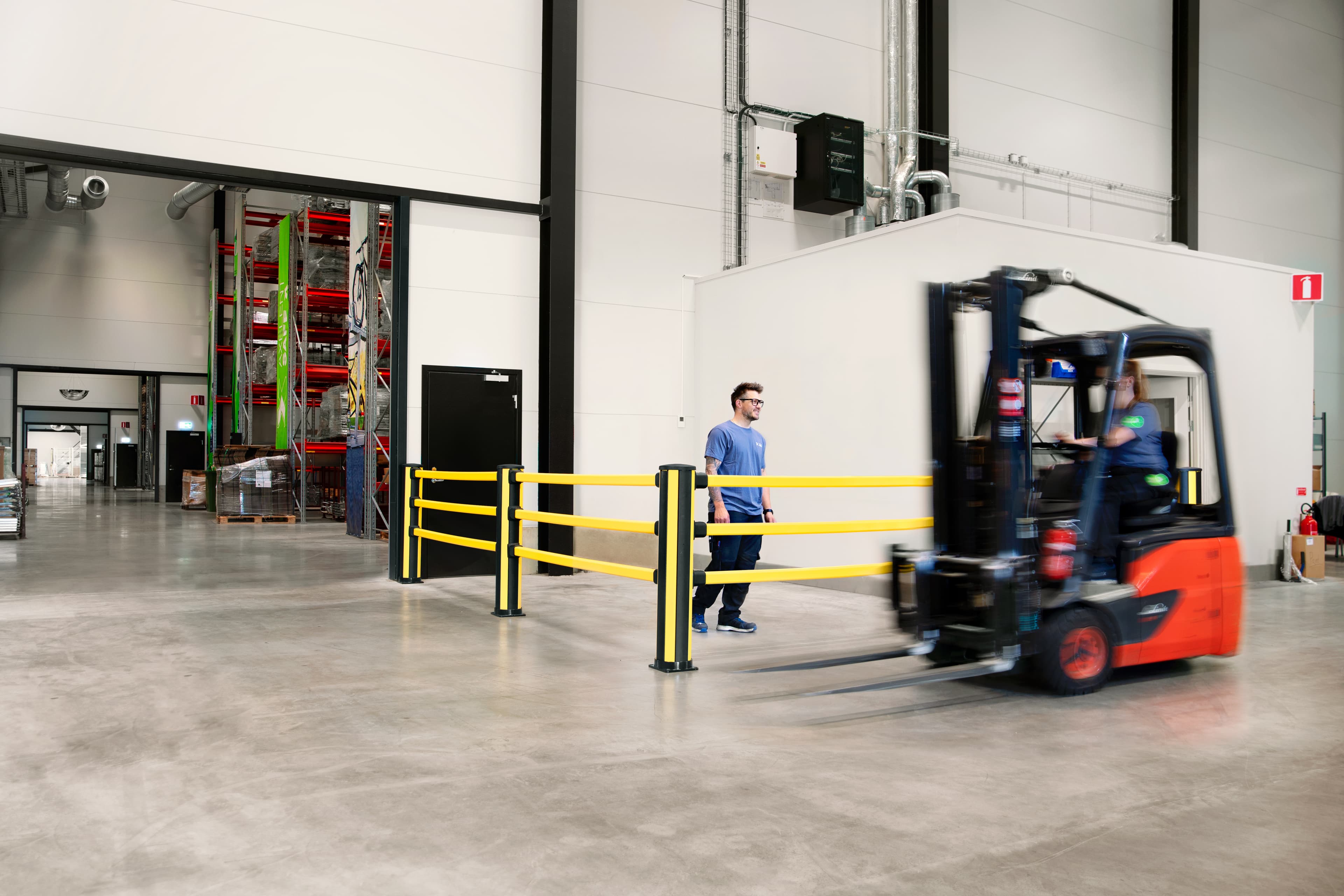 A man is shown walking in a wareohuse environment protected by pedestrian barrier as a forklift truck moves past him.