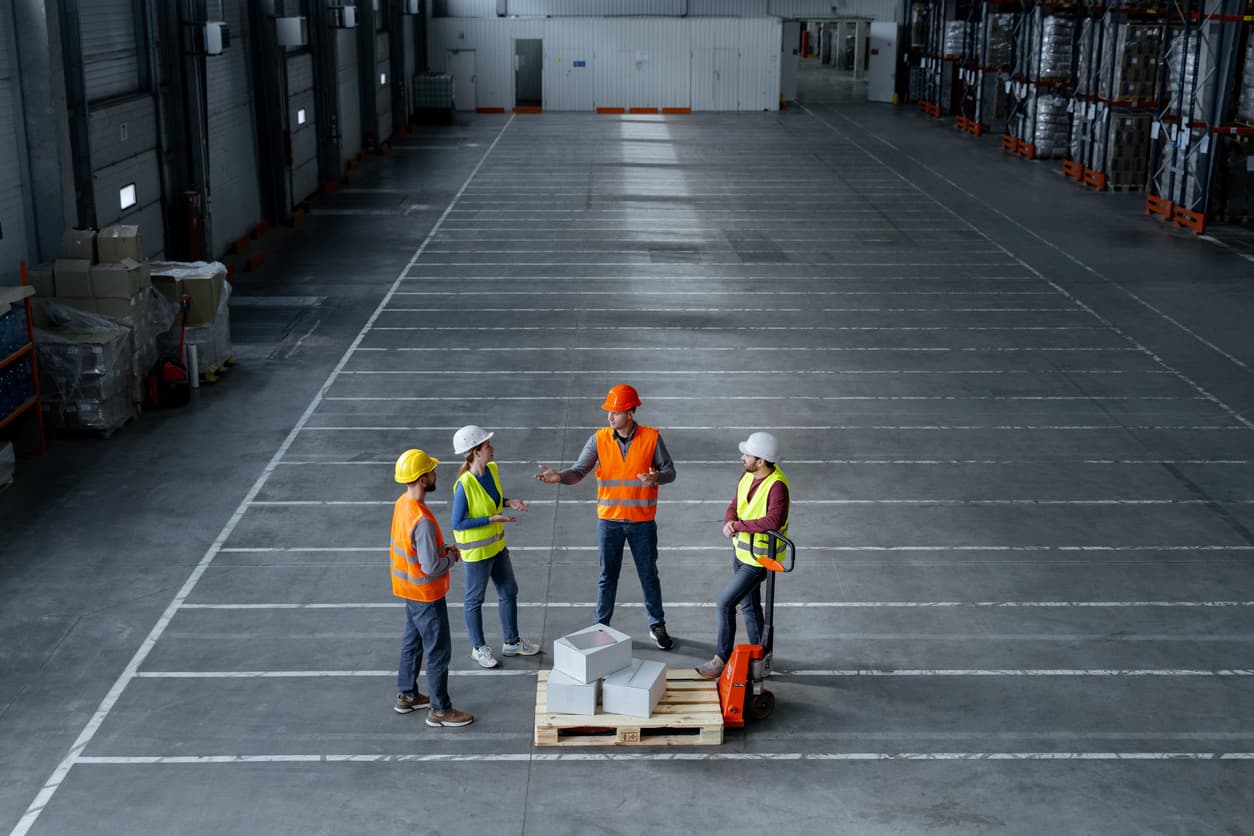 four people are shown talking in a warehouse environment with a pallet truck centrally