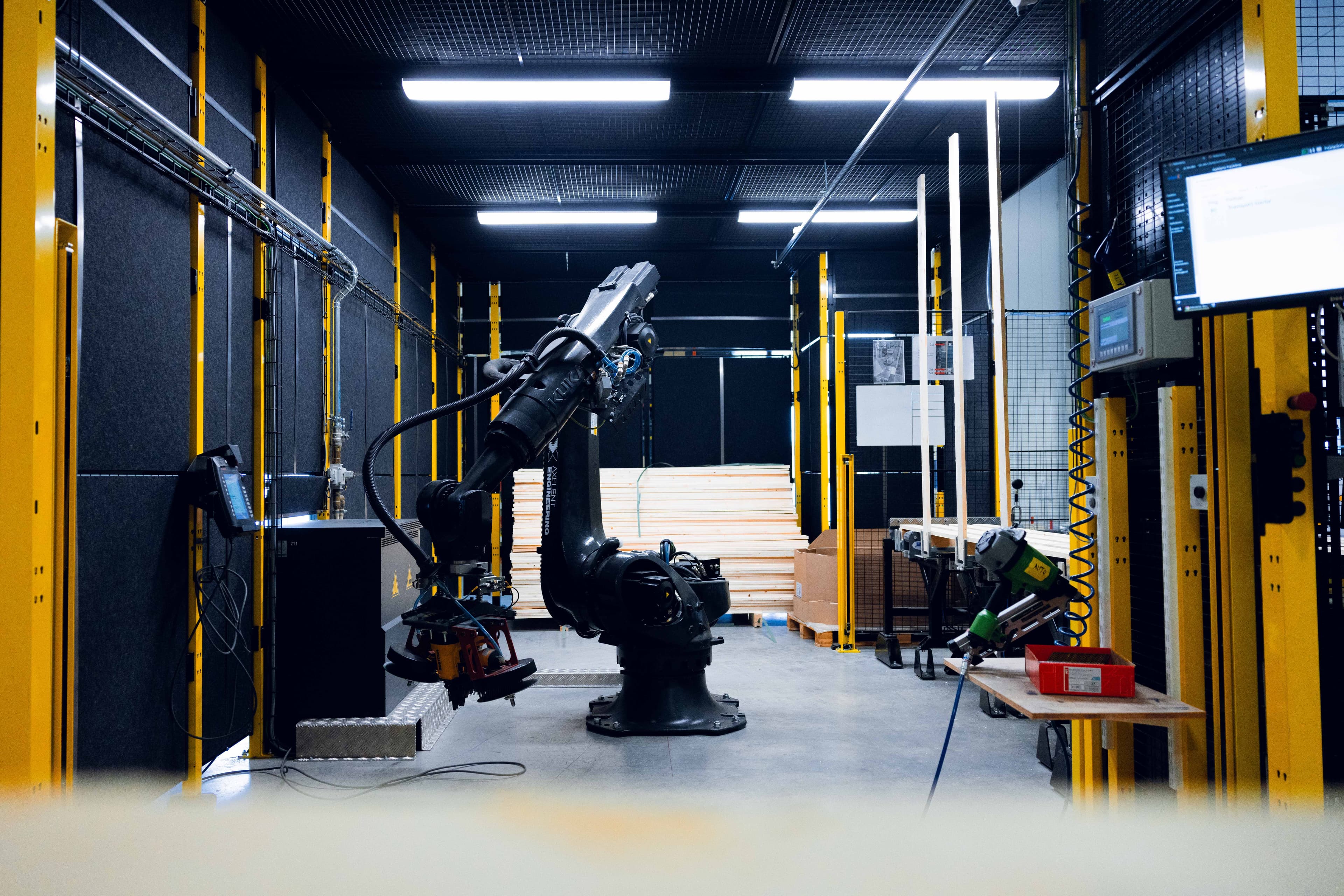 A robotic arm is shown inside an assembly cell for wooden pallets protected by Axelent machine guarding