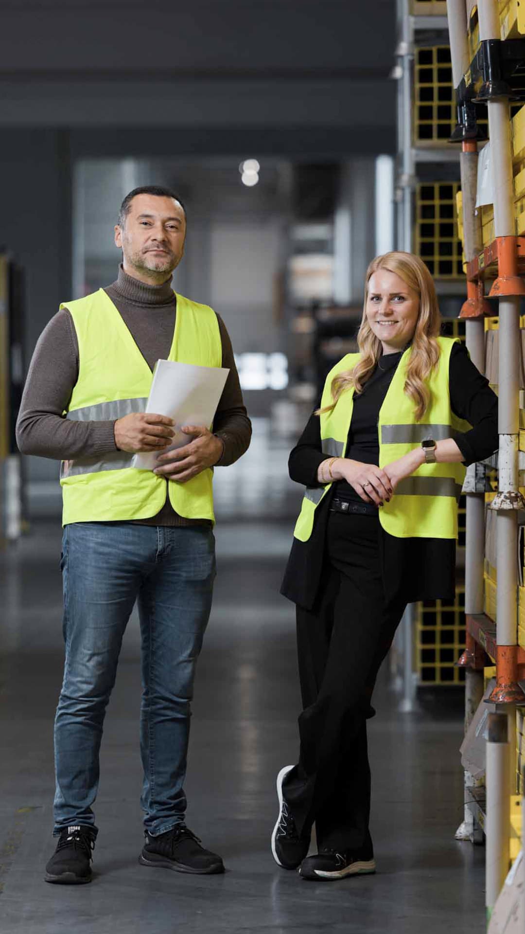 A man and a woman wearing high-visibility vests look into the camera and smile
