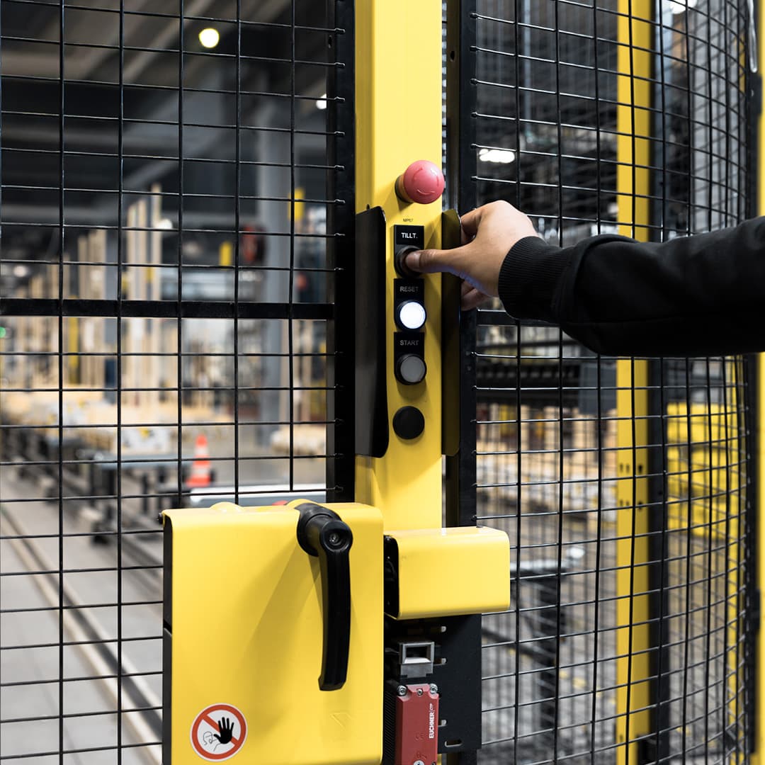 Hand operating a control panel on an industrial machine safety fence