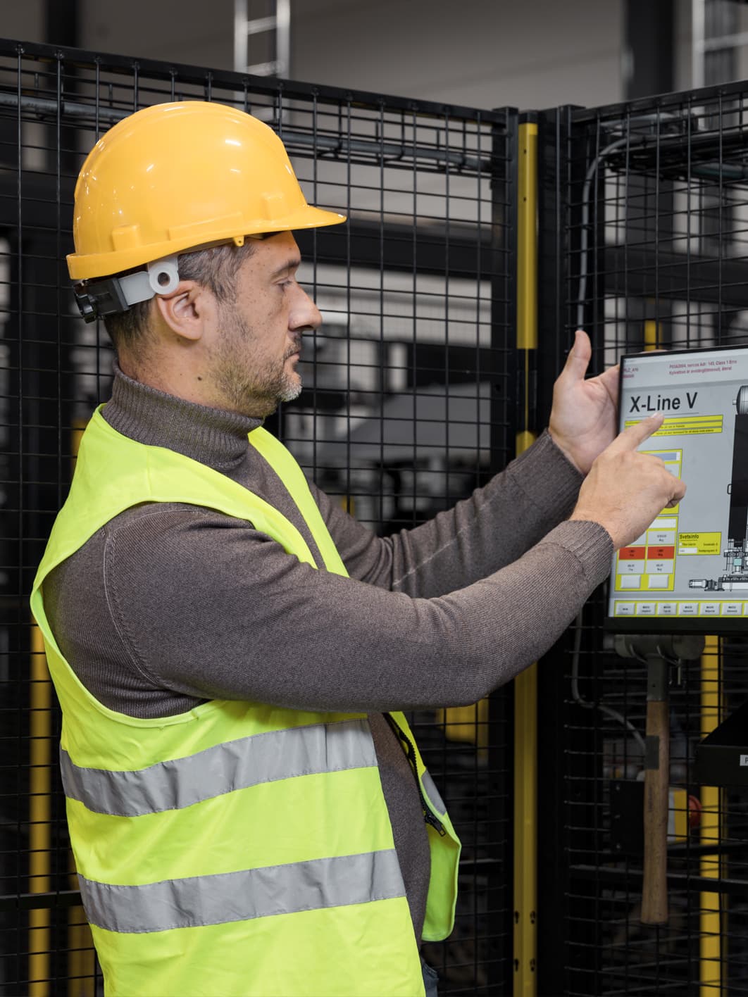 Worker operating a touchscreen control panel beside Axelent machine guarding