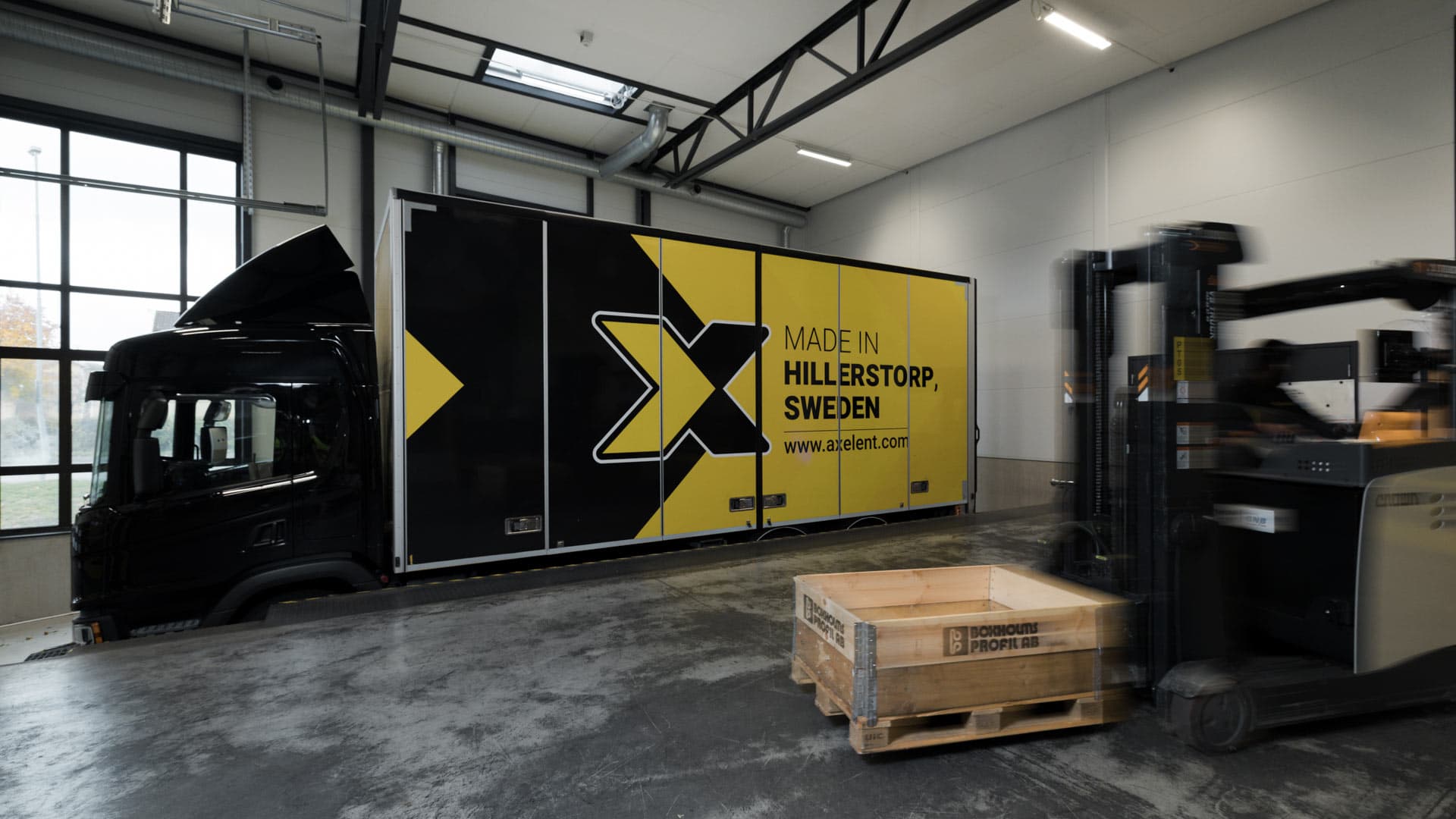 Forklift handling goods inside a warehouse with a branded delivery truck in the background