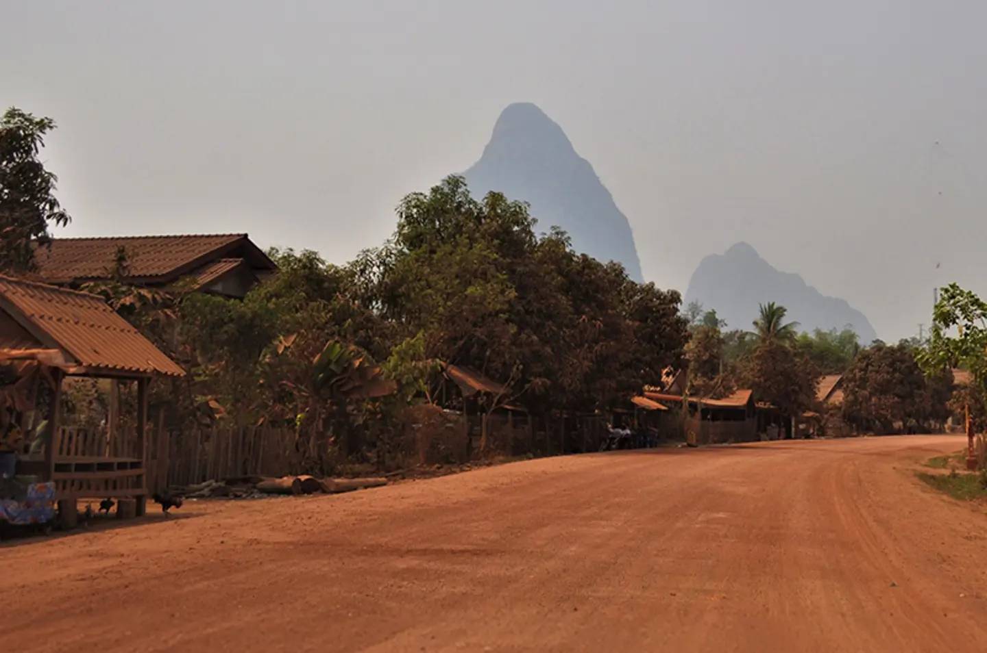 Red gravel road with bushes and mountains in the bakground in Laos