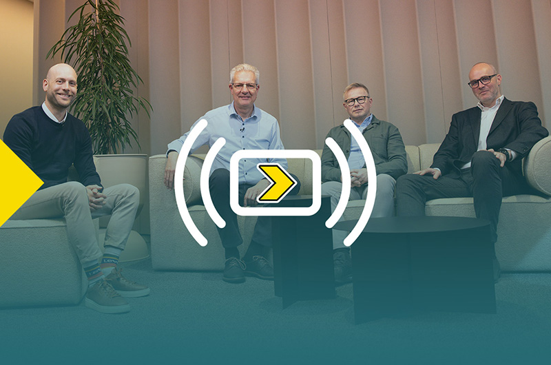 Four men seated on sofas facing the camera. The image has a gradient overlay with the logo for Axelent's webinar "Axelent Goes Live"