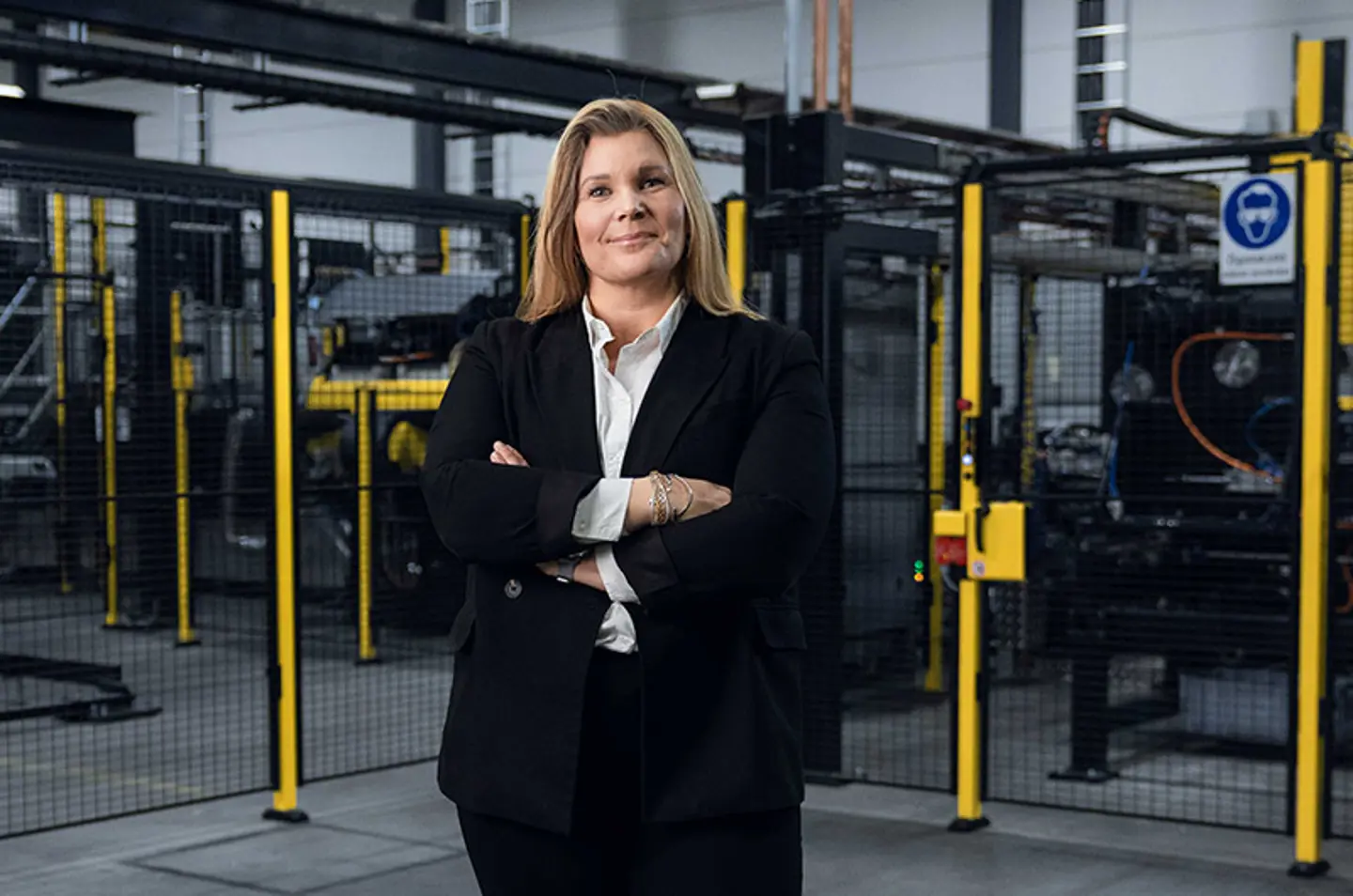 Axelent CEO Karin Sandén Ahlqvist standing with crossed armes infront of an industrial setting with black mesh panels and yellow posts