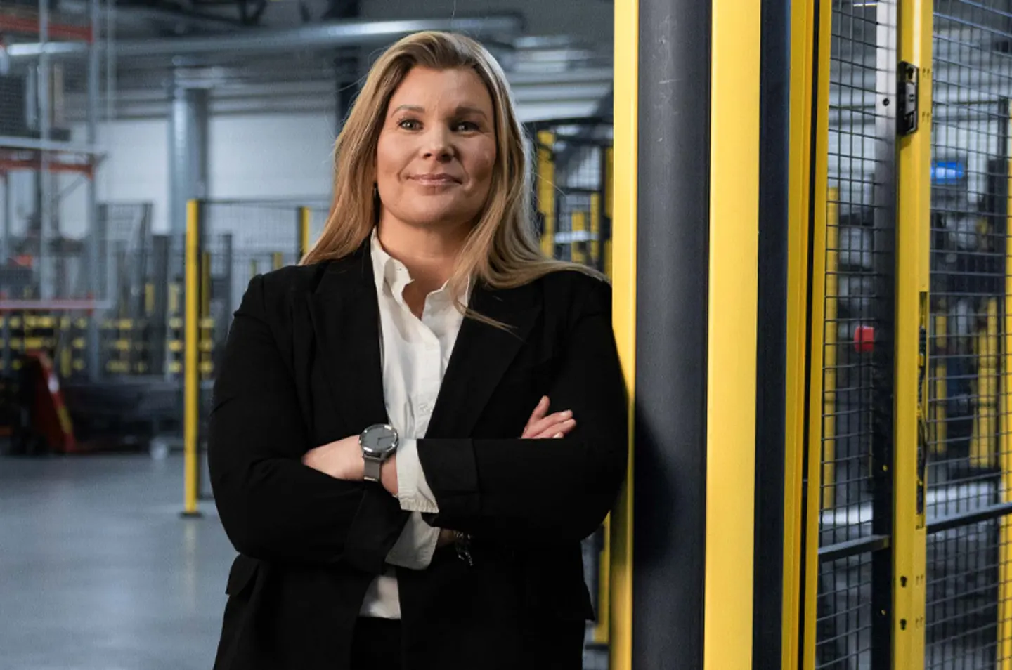 Karin Sanden Ahlqvist, Axelent CEO leaning on a black and yellow bollard with an industrial setting in the background