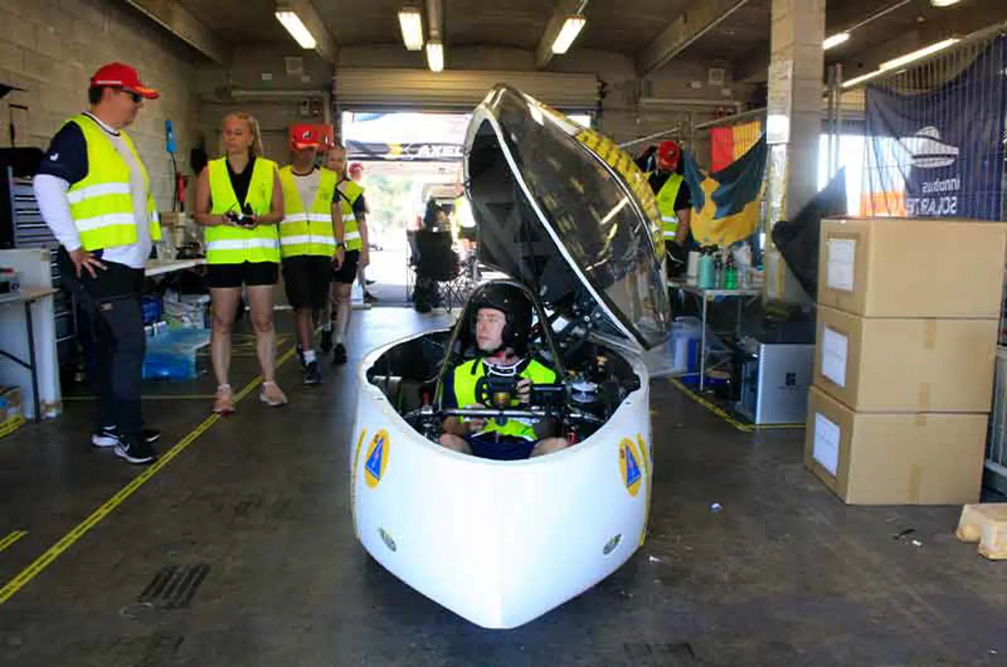 The solar car Nova Lumia in the garage in Hidden Valley, Darwin with members of JU Solar Team 2025 standing around it discussing