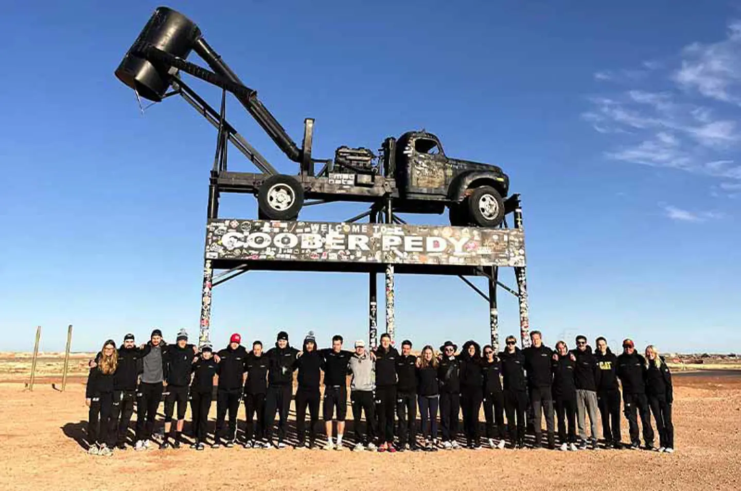 All of the members of JU Solar Team standing infront of the Coobers Pedy sign in Australia