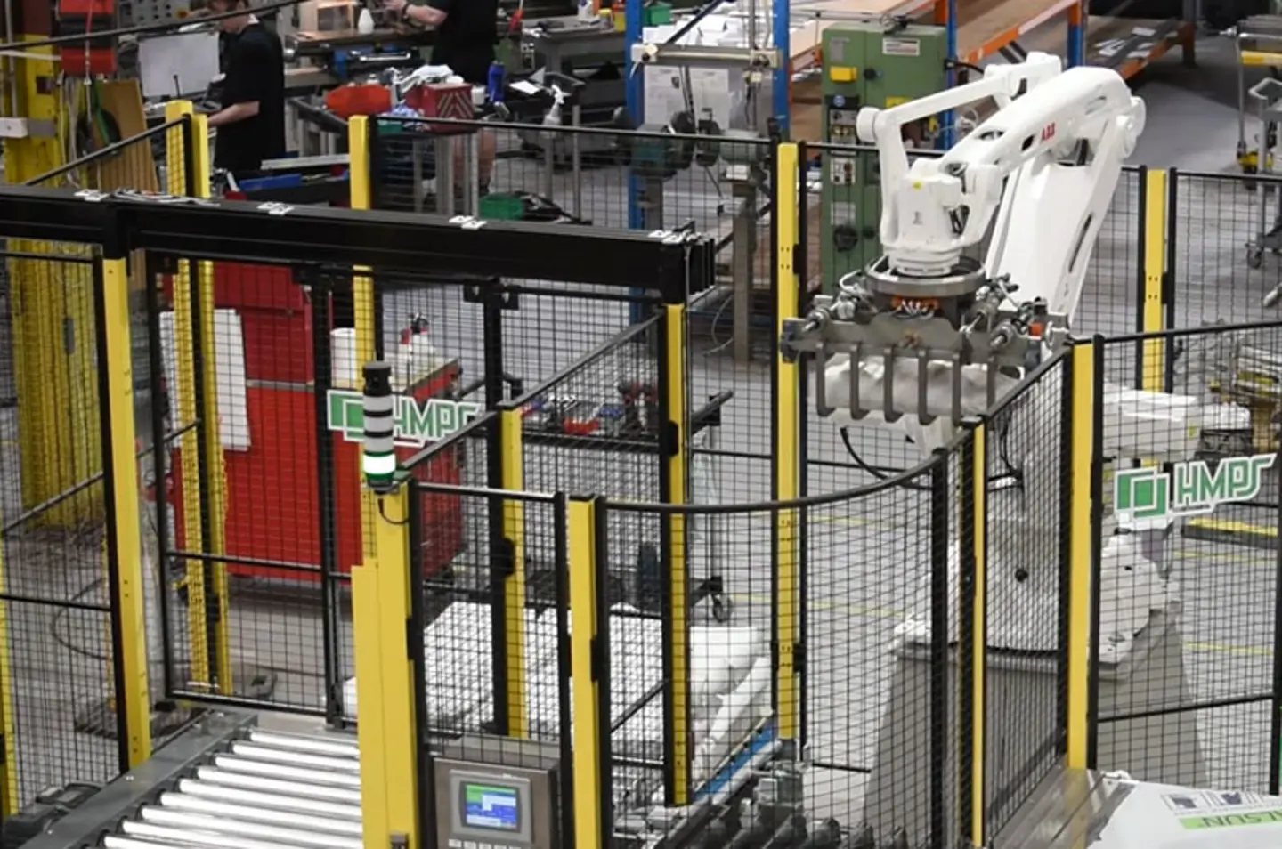 Automated industrial robot arm operating in a factory with conveyor systems and safety fencing